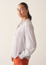 Woman wearing white and blue stripe light shirt with ruffle collar and red linen shorts