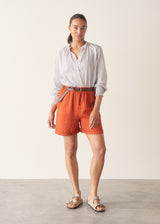 Woman wearing white and blue stripe light shirt with ruffle collar and red linen shorts