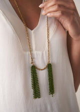 Model wearing a long, chunky chain necklace with two pendants made of colourful green crystal strands, with a white satin top
