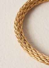 Close up of gold rope style bangle on a beige background